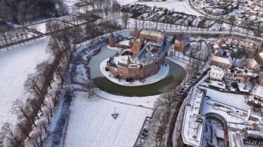 Karlı bir hendekle çevrili dairesel tuğla bir kalenin havadan görünüşü. Kış kasabasında evler, yollar, ağaçlar ve yakınlardaki büyük bir kilise..