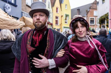Deventer, Overijssel, Hollanda - 14.12.2025: Victoria dönemi kostümlü iki kişi, halka açık bir festival sırasında dekoratif bir sokakta yürüyor.