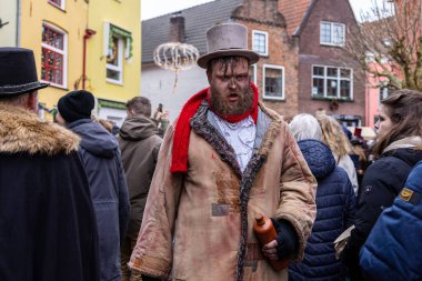 Deventer, Overijssel, Hollanda - 14.12.2025: Yamalı ceket ve silindir şapkalı Viktorya tarzı kostüm giyen bir adam, festival sırasında elinde bir şişe tutuyor.
