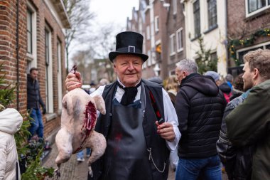 Deventer, Overijssel, Hollanda - 14.12.2025: Kış kalabalığıyla çevrili bir sokak etkinliği sırasında koparılmış bir kuşu ayaklarından tutan tarihi giysili adam.