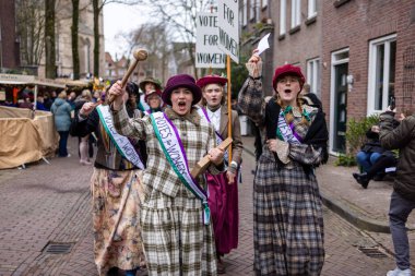 Deventer, Overijssel, Hollanda - 14.12.2025: 20. yüzyılın başlarında kadınlar için giysi yürüyüşü tarihi yeniden canlandırma sırasında kadın kuşağı ve tabelalarıyla.
