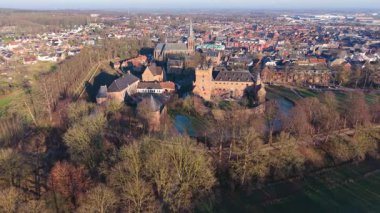 Büyük kırmızı tuğlalı bir kale, kilise kulesi, hendek ve çevresindeki sokaklarla ortaçağ mimarisini modern şehir planıyla harmanlayan tarihi bir Avrupa kasabasının havadan görünüşü..