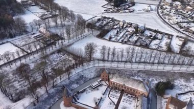 Dağınık evler, ağaçlık yollar, açık araziler ve sakin bir kırsal alan oluşturan sakin kış yolları ile kaplı bir kırsal alanın havadan görünüşü.