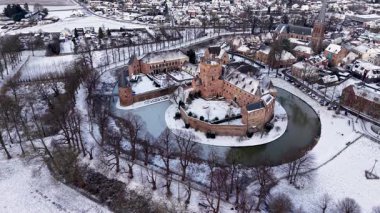 Karla kaplı bir hendekle, kulelerle, duvarlarla, yakınlardaki evlerle ve karla kaplı sessiz bir kasabadaki kilise kulesiyle çevrili tarihi bir şatonun kış manzarası..