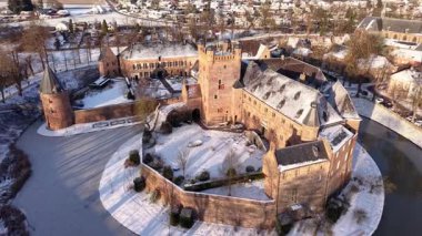 Karla kaplı, kuleleri, avluları ve kırmızı beyaz panjurları olan, sakin, tarihi bir manzarada, ağaçlar ve patikalarla çevrili, kar kaplı bir kalenin kış manzarası..