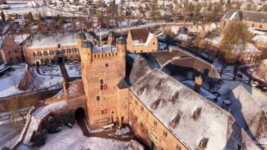 Ağaçlar, yakınlardaki evler ve kiliselerle çevrili, karla kaplı tuğladan kale ve hendekli bir kalenin kış manzarası dingin ve pitoresk tarihi bir manzara oluşturuyor..