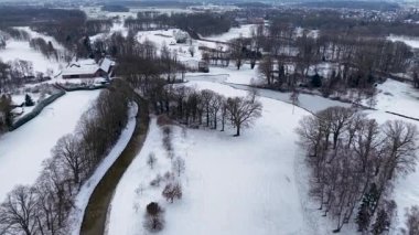 Karlı tarlalar ve ormanlar arasında akan kıvrımlı bir nehrin kış manzarası, dağınık evler ve uzak bir kasaba, sakin, geniş bir kış manzarası yaratıyor..