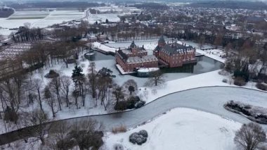 Karlı tarlalar, donmuş su yolları, yapraksız ağaçlar ve arazi boyunca uzanan uzak bir kasaba ile çevrili kuleleri ve hendeği olan büyük kırmızı tuğladan bir kalenin havadan görünüşü..