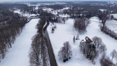 Karlı tarlalar ve ormanlar arasında akan kıvrımlı bir nehrin kış manzarası, dağınık evler ve uzak bir kasaba, sakin, geniş bir kış manzarası yaratıyor..