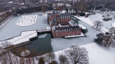 Kızıl tuğladan bir şatonun havadan görünüşü, kuleleri ve hendeği olan, karla kaplı resmi bir bahçenin yanında, ağaçlarla çevrili ve yakınlardaki bir kasaba, dingin, beyaz bir manzara..