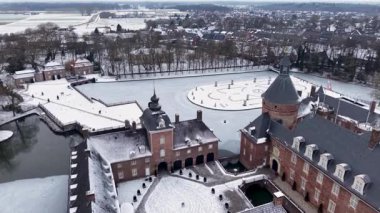 Kuleleri, karlı bir avlusu, donmuş bir hendeği, buzun üzerinde dairesel bir bahçesi ve çevresi tarlalarla çevrili kasaba binaları olan kırmızı tuğladan bir şatonun havadan görünüşü..