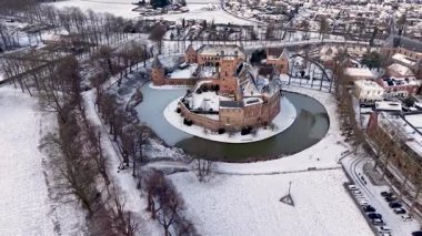 Avrupa 'nın karlı topraklarında tarihi bir şatonun çarpıcı kış havası. Kalede taş kuleler ve buzlu ağaçlar ve beyaz tarlalarla çevrili dairesel donmuş bir hendek bulunuyor..