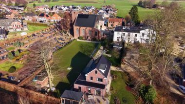 Güneş ışığı yeşil alanların kenarındaki huzurlu bir Avrupa köyünü ve tuğla kilisesini aydınlatıyor. Hava manzarası, güneş panelleri ve öğleden sonra tarihi mezarlığı olan modern evleri yakalıyor..