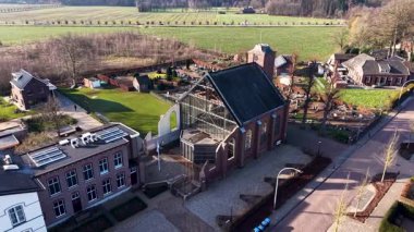 Güneş ışığı, modern cam genişletme ile benzersiz bir tuğla kiliseyi aydınlatan bir Avrupa köyünü yıkıyor. Hava manzarası düzenli yerleşim caddelerini, güneş panellerini ve tarihi bir mezarlığı yakalıyor..