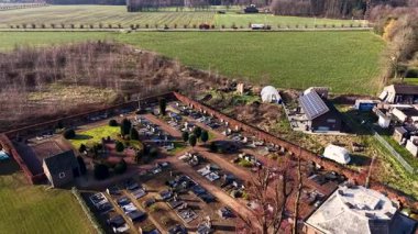 Modern cam bir ek bina ile tarihi tuğla bir kilisenin yer aldığı huzurlu bir Avrupa köyünün havadan görünüşü. Güneş panelli çatıları olan düzenli yerleşim sokakları yerel bir mezarlık ve yeşil tarlalarla sınırdır.