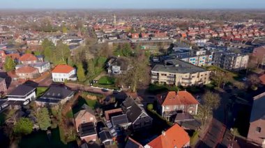 Klasik tuğladan evler, kırmızı kiremitli çatılar, özel bahçeler ve açık bir öğleden sonra gökyüzü altında bir kilise olan temiz bir Avrupa banliyö mahallesinin insansız hava aracı perspektifi..