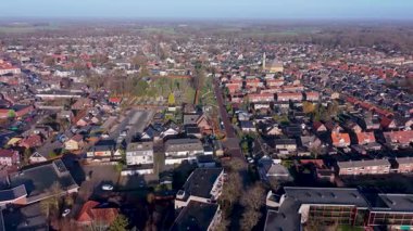 Açık bir sabah gökyüzü altında geleneksel kırmızı kiremitli çatılar, tuğla evler, yerel bir kilise ve yeşil banliyö manzaralı huzurlu bir Hollanda kasabasının yüksek açılı manzarası.