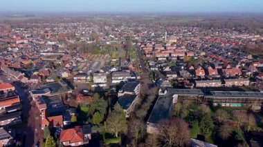 Açık bir sabah gökyüzü altında geleneksel kırmızı kiremitli çatılar, tuğla evler, yerel bir kilise ve yeşil banliyö manzaralı huzurlu bir Hollanda kasabasının yüksek açılı manzarası.