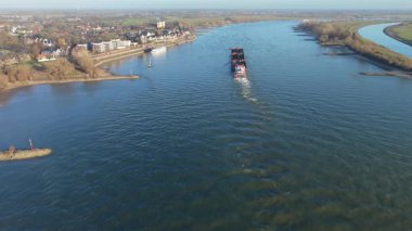 Geniş bir nehirde yol alan iki büyük kargo gemisinin havadan görüntüsü. Çimenli bankalar, küçük yarımadalar ve çevresi yeşil tarlalarla çevrili bir kasaba ve sakin bir kırsal alanda dağınık evler..