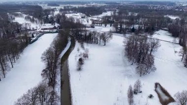 Karlı tarlalar ve ormanlar arasında akan kıvrımlı bir nehrin kış manzarası, dağınık evler ve uzak bir kasaba, sakin, geniş bir kış manzarası yaratıyor..