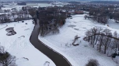 Karlı tarlalar ve ormanlar arasında akan kıvrımlı bir nehrin kış manzarası, dağınık evler ve uzak bir kasaba, sakin, geniş bir kış manzarası yaratıyor..