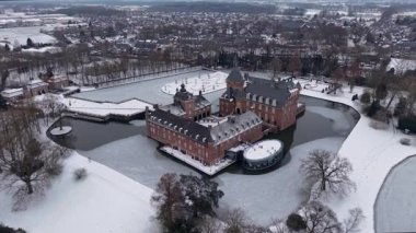 Karlı tarlalar, donmuş su yolları, yapraksız ağaçlar ve arazi boyunca uzanan uzak bir kasaba ile çevrili kuleleri ve hendeği olan büyük kırmızı tuğladan bir kalenin havadan görünüşü..