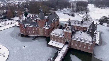 Anholt Kalesi 'nin kışın havadan görünüşü. Karla kaplı çatıları olan kırmızı tuğladan bir mimari hendeğin üzerinde taş bir köprü ve donmuş suyun üzerinde modern oval cam bir pavyon..