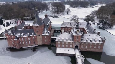 Kış boyunca Almanya 'daki Anholt Kalesi' nin sinematik görüntüsü. Büyük bir kulesi ve avlusu olan tarihi kırmızı tuğladan bir saray. Donmuş hendek ve karla kaplı park manzarasıyla çevrili..