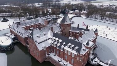 Anholt 'un Almanya' da kış mevsiminde çekilen hava görüntüleri, genişleyen kırmızı tuğla binalarını, avlusunu ve donmuş su ve kar altında ağaçlarla çevrili kulesini gün ışığında gösteriyor..