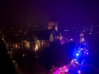 Hollanda, Kampen 'deki Nieuwe Toren kulesinin gece görüşü, maviyle aydınlatılmış. Tarihi şehir, aşağıdaki sokaklarda parlayan şenlikli Noel piyasa ışıklarıyla sisle kaplı..