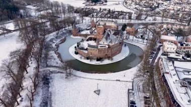 Kışın donmuş bir hendekle çevrili tarihi bir ortaçağ kalesinin çarpıcı hava manzarası. Karla kaplı manzara, çıplak ağaçlar ve geleneksel mimari büyülü bir soğuk mevsimi atmosferi yaratır..