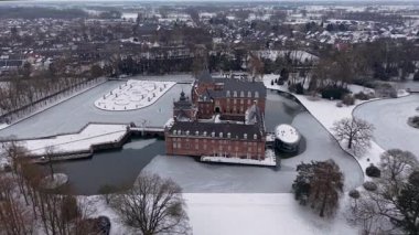 Almanya 'daki tarihi hendekli Burg Anholt şatosunun kışın havadan görünüşü. Ortaçağ tuğla mimarisi. Donmuş bir göl ve manzaralı bir kasaba parkında karla kaplı bahçelerle çevrili kuleleri var..