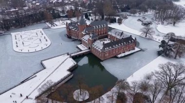 Almanya 'daki Ortaçağ Burg Anholt kalesinin hava görüntüsü. Tuğla kale, donmuş bir hendek ve kışın gökyüzünün altında karla kaplı bahçelerle çevrilidir. Kışın çarpıcı tarihi mimari.