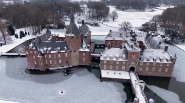 Almanya 'daki Burg Anholt kalesine yakın çekim. Ortaçağ tuğla mimarisi, kuleleri ve donmuş bir hendeğin üzerinde asma köprüsü var. Karlı bir parkla çevrili tarihi bir yer..