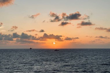 Deniz 'de güzel bir gün batımı. Açık deniz kuyusu peronu ve dramatik bir tonda ikmal botu..