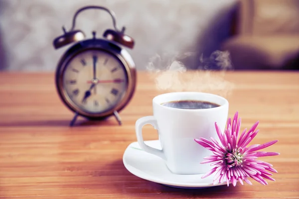 Una taza de café y un reloj despertador en el fondo en la mesa de madera, procesamiento cruzado — Foto de Stock
