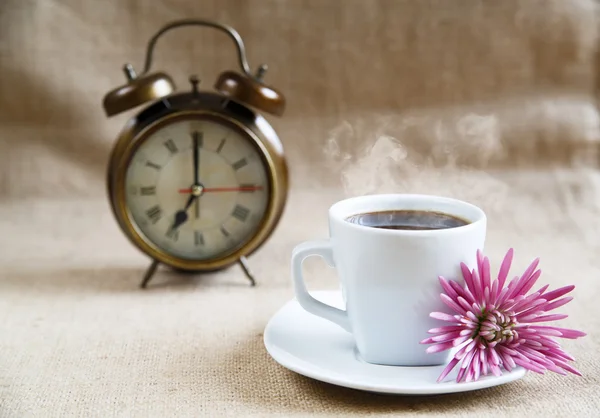 Una taza de café con flor y un despertador en el fondo — Foto de Stock