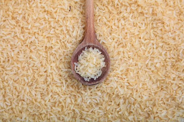 Wooden spoon and parboiled rice background — Stock Photo, Image