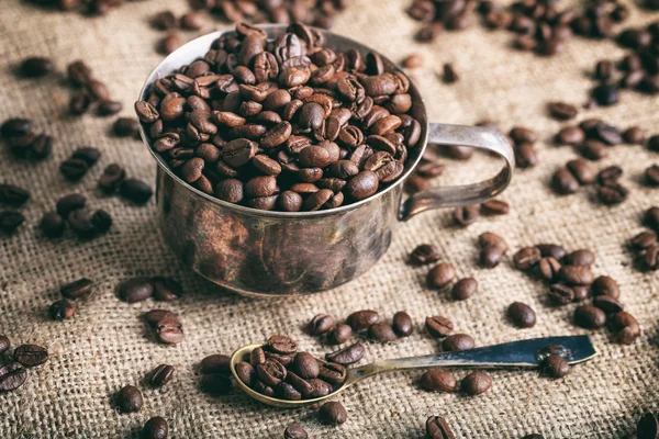 Grãos de café e uma xícara em uma serapilheira — Fotografia de Stock