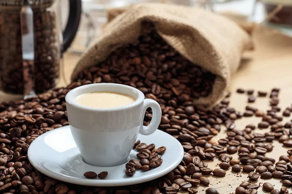 Кофейные зерна из мешка и чашка кофе — стоковое фото