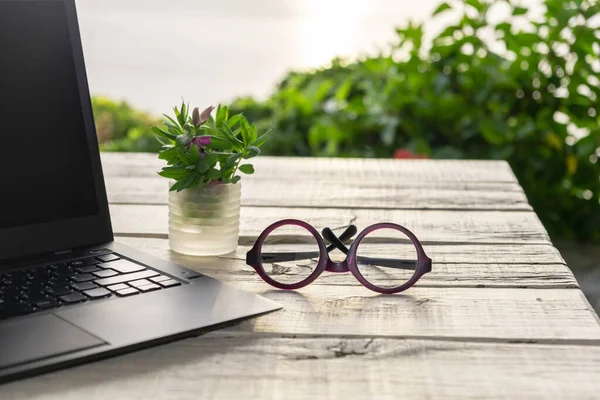 Outdoor office desk, computer laptop in the garden, glasses on the table, green nature background, quarantine home office concept