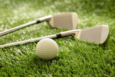 Golf topu ve golf sopaları yeşil sahada, güneş ışığı yansımaları, yakın görüş. Golf malzemeleri ve ekipman konsepti.