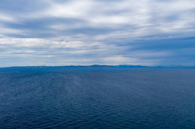Dalgalı deniz ve bulutlu gökyüzü. Suyun üzerinde ağır bulutlar ve arka planda dağlar. Akdeniz, Kea, Tzia Adası, Yunanistan 'da yelkenliler yarışıyor. 