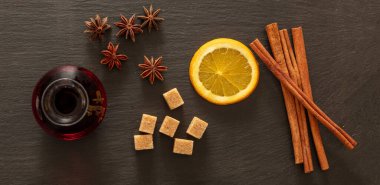Sıcak şarap tarifi malzemeleri, Noel kışı sıcak alkol içeceği. Turuncu, tarçın çubukları, yıldız anasonu ve siyah taşın üzerindeki şeker, üst manzara.