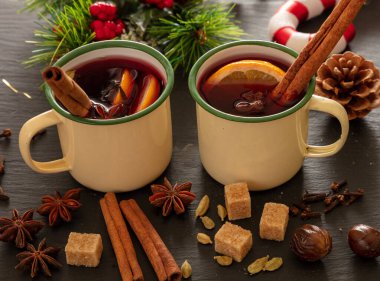 Sıcak şarap, kışın ısınan alkol içeceği, iki eski bardak, portakal ve baharatlar ve siyah taşın üzerine Noel süslemesi, yakın çekim..