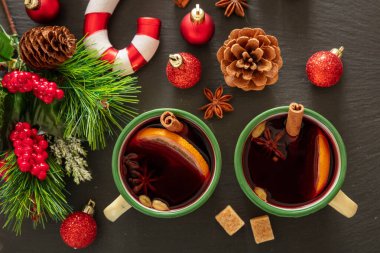 Sıcak şarap, kışın ısınan alkol, iki eski bardak, portakal ve baharatlar ve siyah taşın üzerine Noel süslemesi, yakın çekim..
