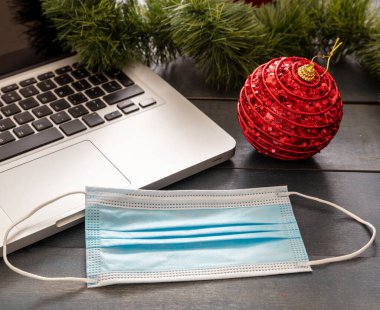 Noel tecridi, ofis kapalı, covid 19 salgını. Mavi ahşap arka planda koruyucu maske ve xmas süsleri mevsim tatil masası.
