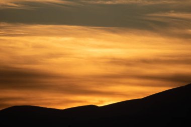 Renkli gökyüzünde gün doğumu, günbatımı. Altın güneş ışınları ufku aydınlatıyor. Bulutların arasından geçen güneş, dağların üzerinden geçen siluet, arka plan bulutları. Duvar kağıdı, kart.
