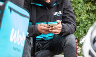Atina, Yunanistan. 12 Kasım 2020. Wolt yemek dağıtım servisi, konteynır kutusunun yanında oturan kurye cep telefonunu kontrol ediyor.
