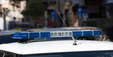 Polis arabasında mavi ışık, yakın çekim, bulanık şehir manzarası. Çatıya ışık çubuğu ve siren monte edildi. Acil durum aracı, belediye polisi.